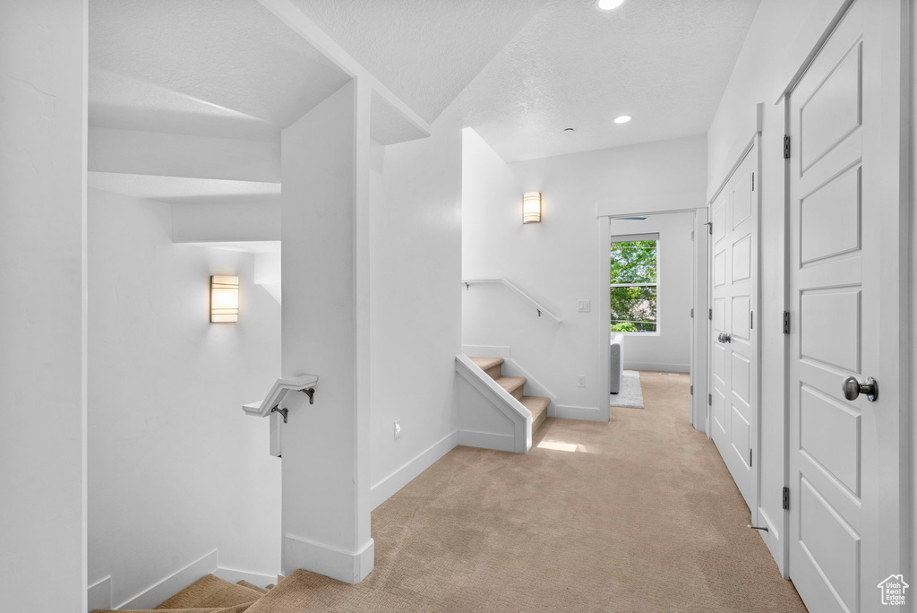 Corridor with light colored carpet, baseboards, recessed lighting, stairs, and a textured ceiling
