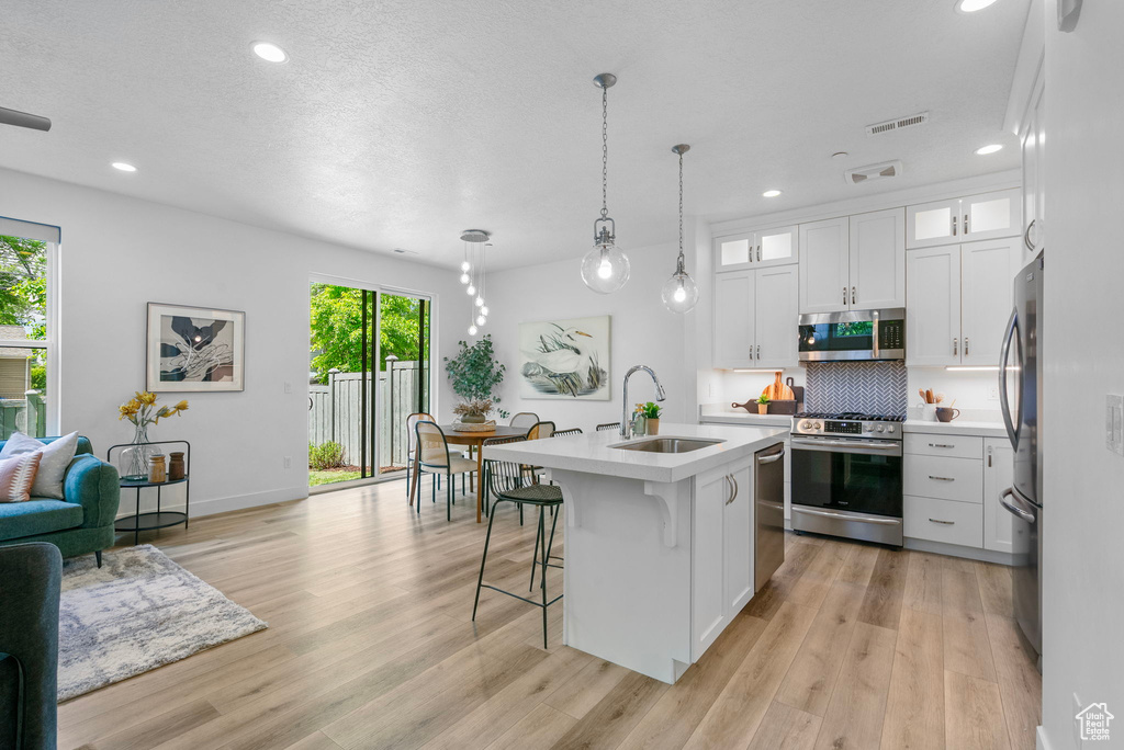 Kitchen with stainless steel appliances, a sink, light countertops, recessed lighting, and light wood-style floors