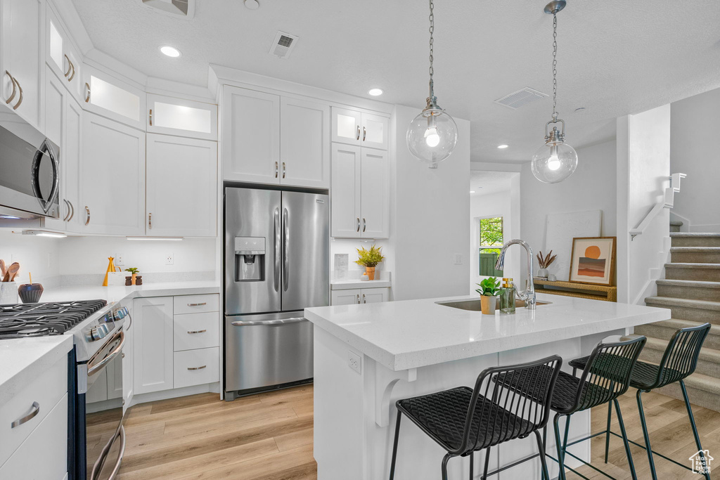 Kitchen with stainless steel appliances, light wood finished floors, a sink, light countertops, and recessed lighting