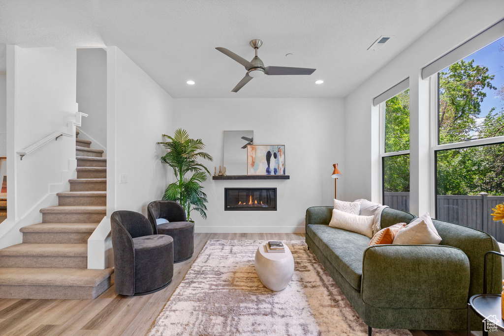 Living area with wood finished floors, stairs, a glass covered fireplace, ceiling fan, and recessed lighting