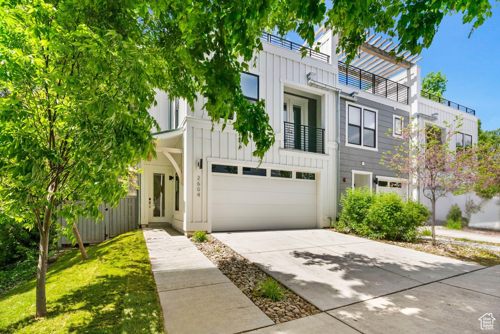 Townhome / multi-family property featuring board and batten siding, concrete driveway, a garage, a pergola, and a balcony