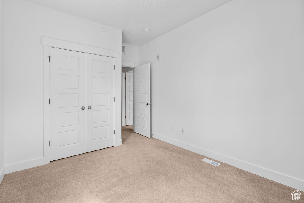 Unfurnished bedroom with light carpet, a closet, and baseboards