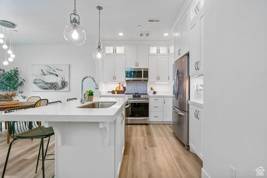 Kitchen featuring appliances with stainless steel finishes, a sink, light countertops, a kitchen bar, and light wood-style flooring