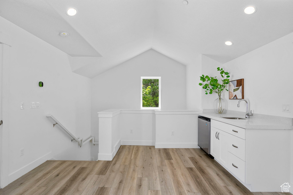 Kitchen with a sink, dishwasher, light countertops, lofted ceiling, and white cabinetry