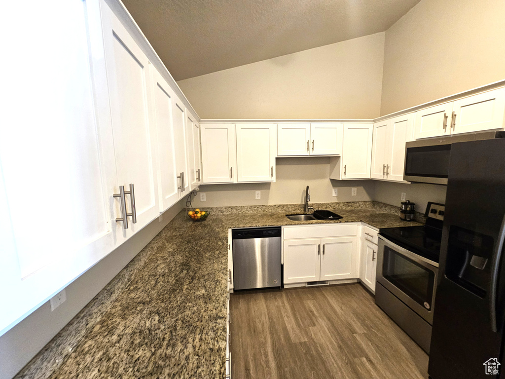 Kitchen with stainless steel appliances, a sink, white cabinets, lofted ceiling, and dark wood-type flooring