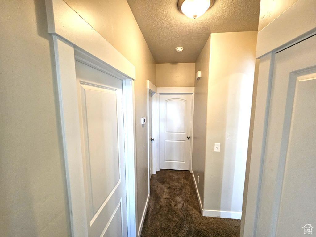 Corridor with a textured ceiling, baseboards, and dark carpet
