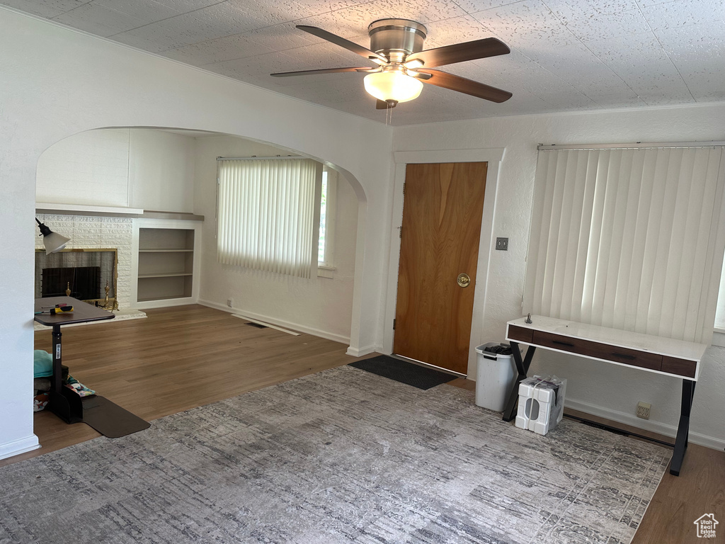 Unfurnished living room with wood finished floors, ceiling fan, a fireplace, arched walkways, and baseboards