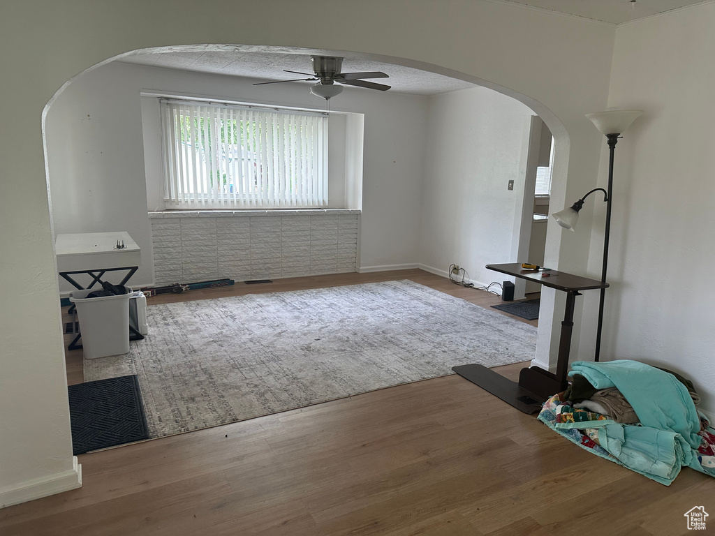 Unfurnished living room featuring arched walkways, ceiling fan, wood finished floors, and baseboards
