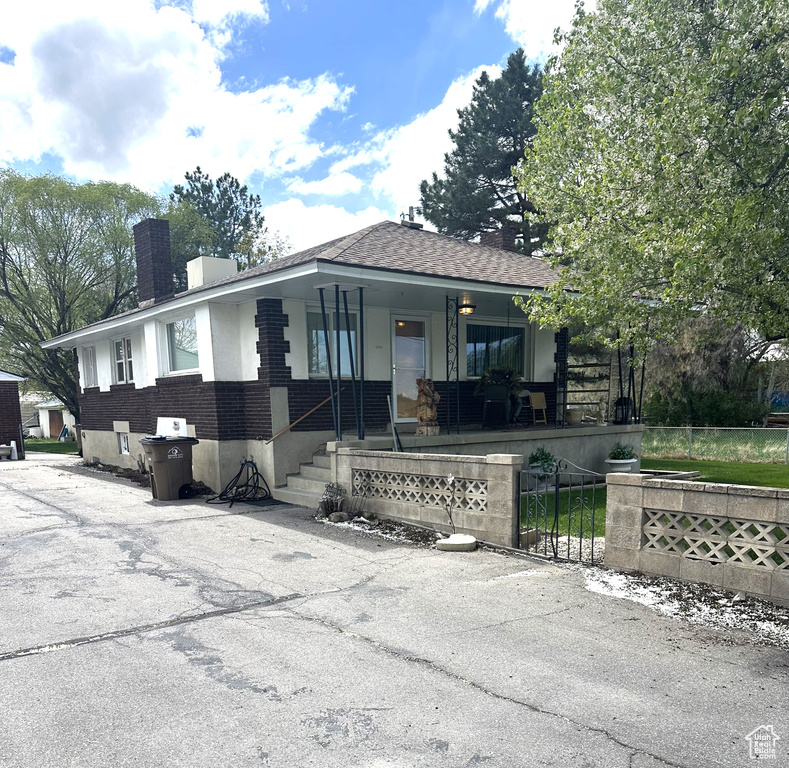 View of front of house featuring a porch, a chimney, a fenced front yard, brick siding, and a shingled roof