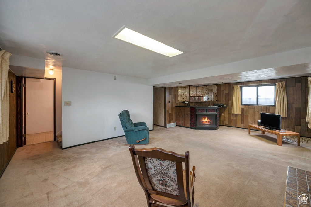 Living room featuring light carpet, a warm lit fireplace, and wood walls