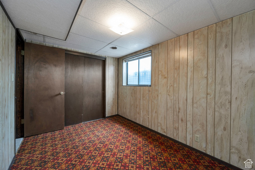 Unfurnished bedroom with wooden walls, a drop ceiling, a closet, and carpet floors