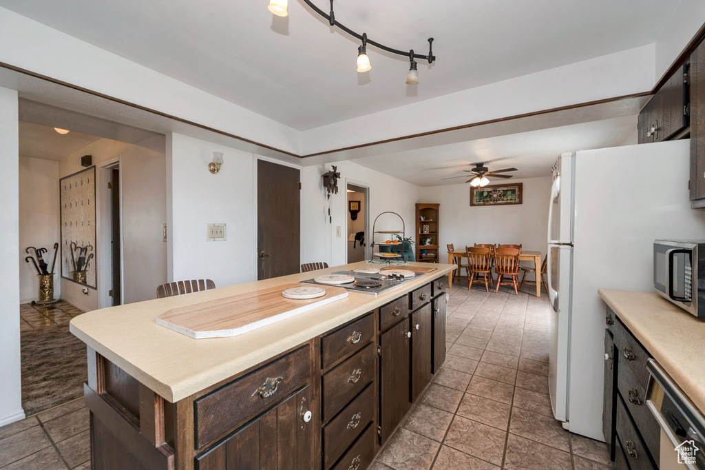 Kitchen with appliances with stainless steel finishes, light countertops, ceiling fan, dark brown cabinetry, and a center island