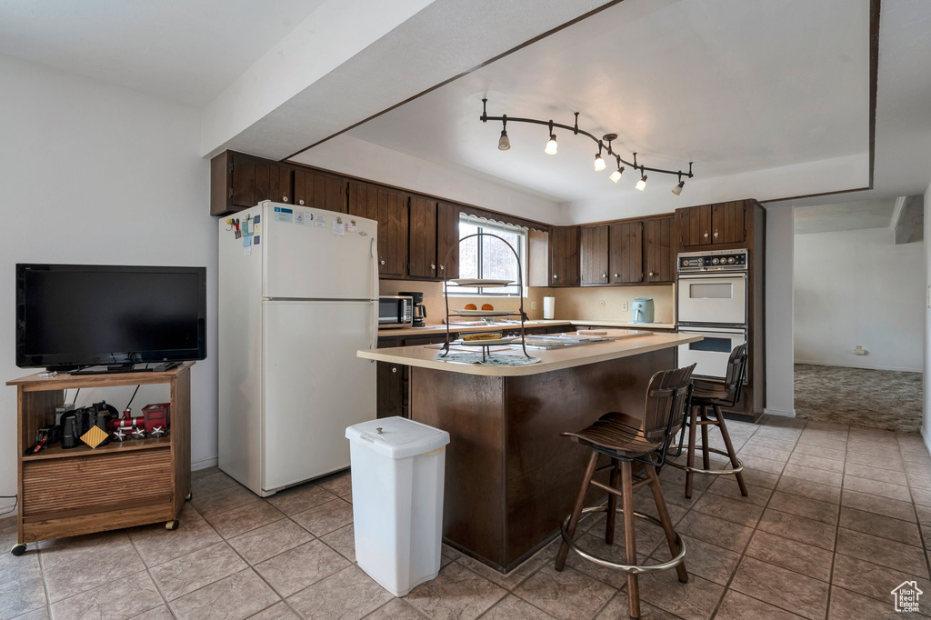 Kitchen with white appliances, dark brown cabinetry, light countertops, and a kitchen island