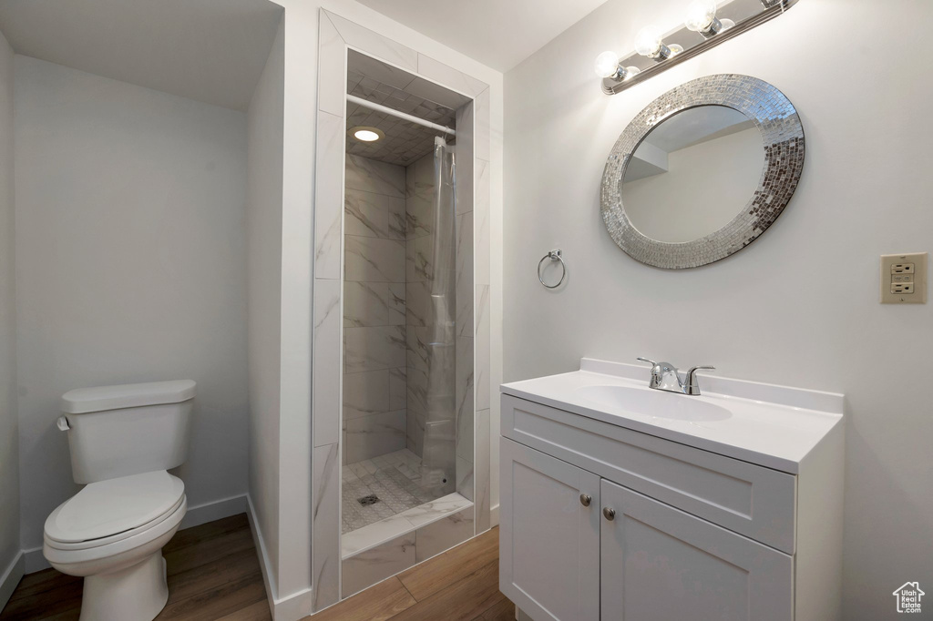Full bath with wood finished floors, toilet, a stall shower, vanity, and baseboards