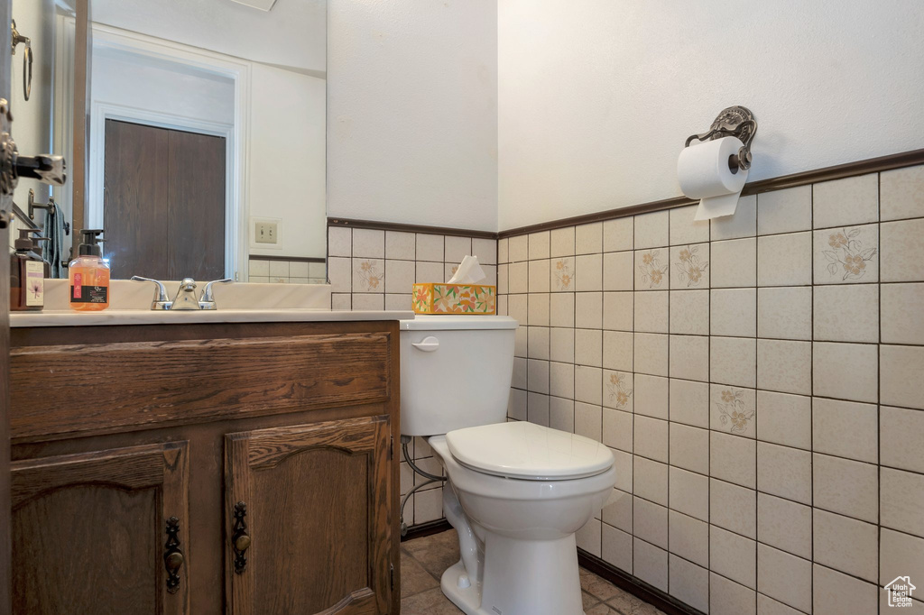 Half bath with toilet, tile walls, vanity, and a wainscoted wall