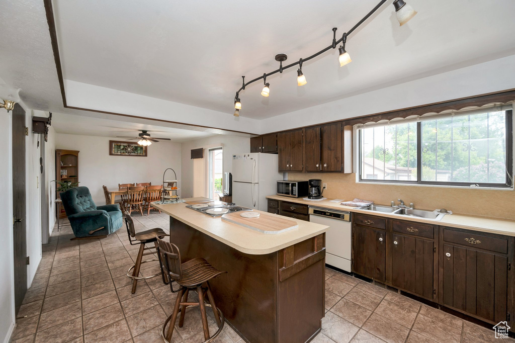 Kitchen featuring white appliances, a kitchen bar, a sink, dark brown cabinetry, and light countertops