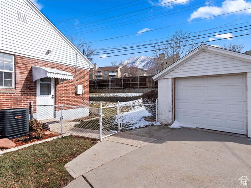 View of side of home featuring brick siding, fence, an outbuilding, driveway, and cooling unit