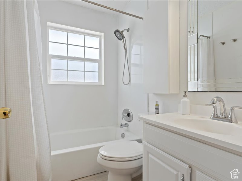 Bathroom featuring toilet, shower / bathtub combination with curtain, and vanity