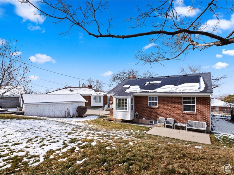 Snow covered back of property with solar panels, a chimney, a patio, and brick siding