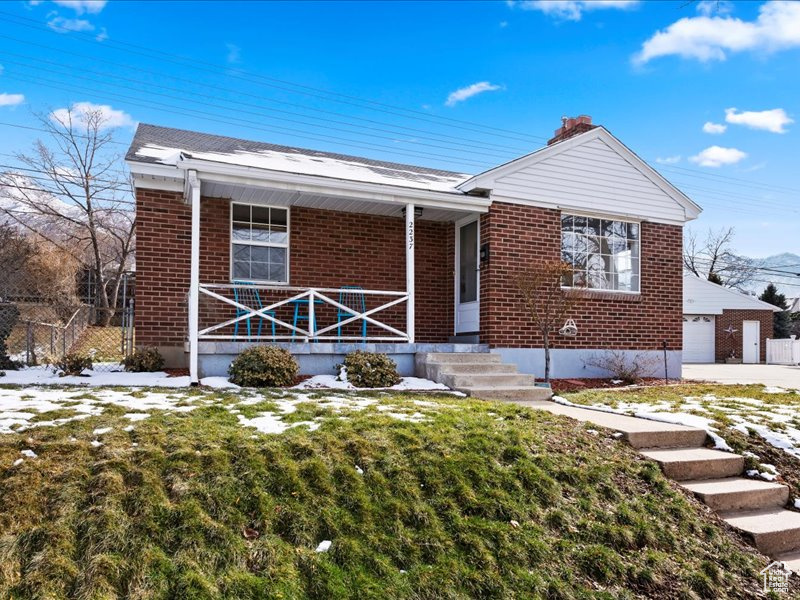 View of front of home with a front yard, brick siding, covered porch, a chimney, and fence
