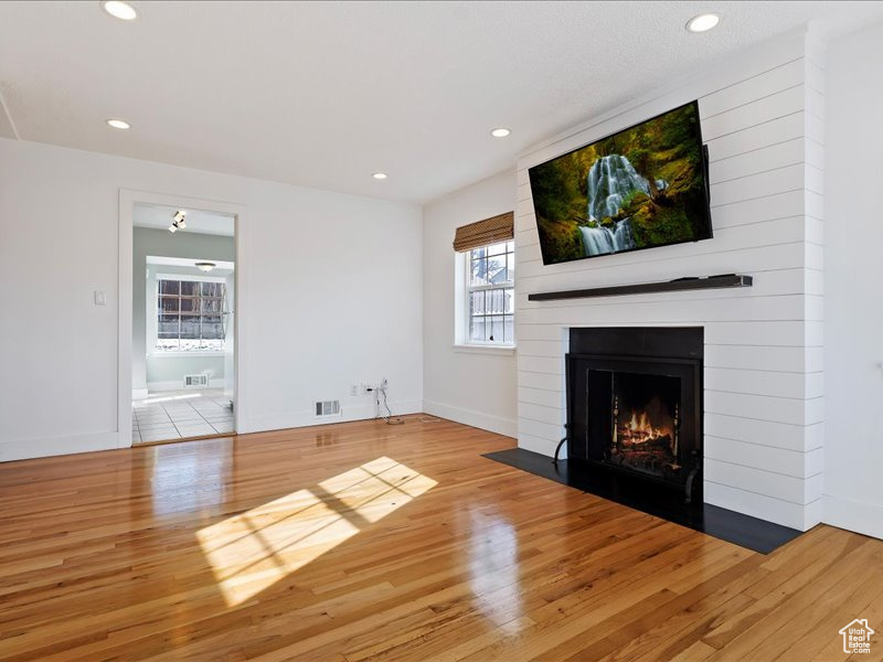 Unfurnished living room with recessed lighting, wood finished floors, a fireplace, baseboards, and visible vents