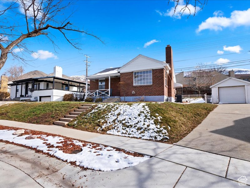 Single story home with a chimney, covered porch, brick siding, driveway, and a detached garage