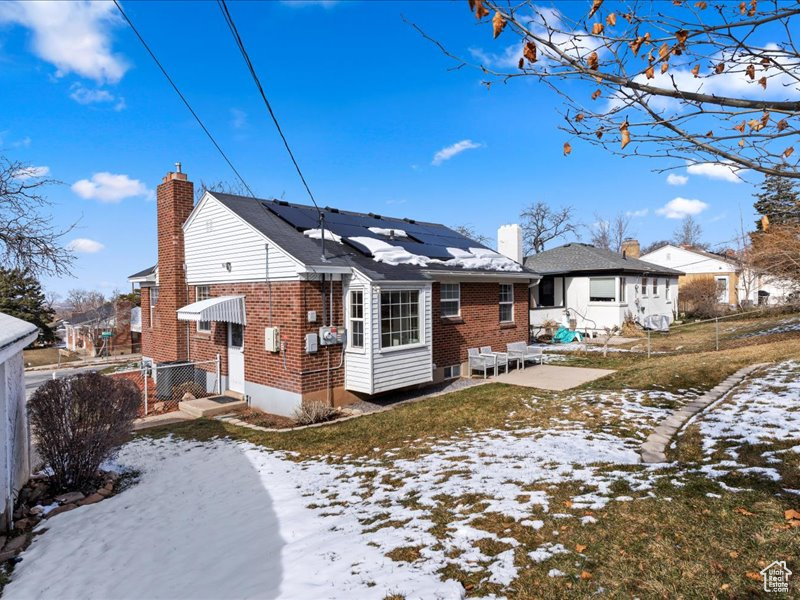 Snow covered back of property with roof mounted solar panels, a chimney, and brick siding