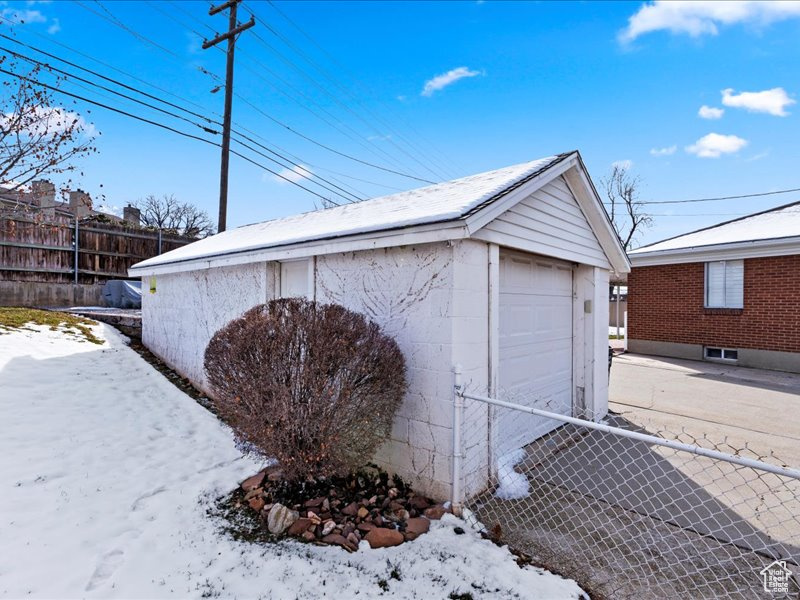 Snow covered garage with a detached garage and fence