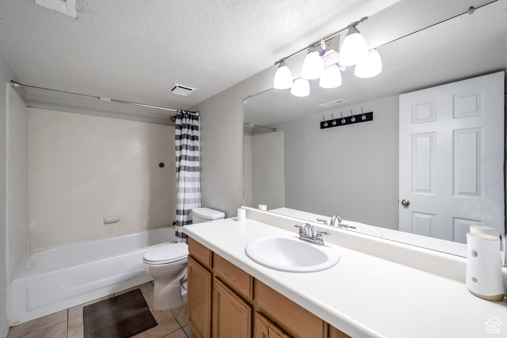 Bathroom featuring toilet, shower / bath combo, vanity, a textured ceiling, and tile patterned floors