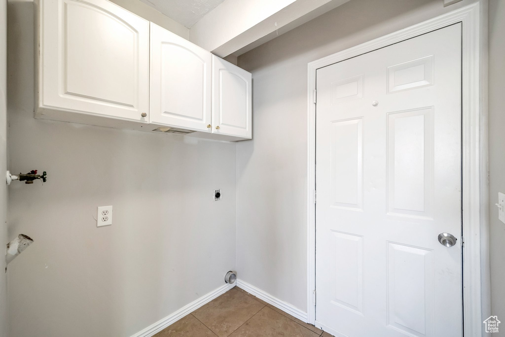 Clothes washing area featuring electric dryer hookup, baseboards, cabinet space, light tile patterned flooring, and washer hookup