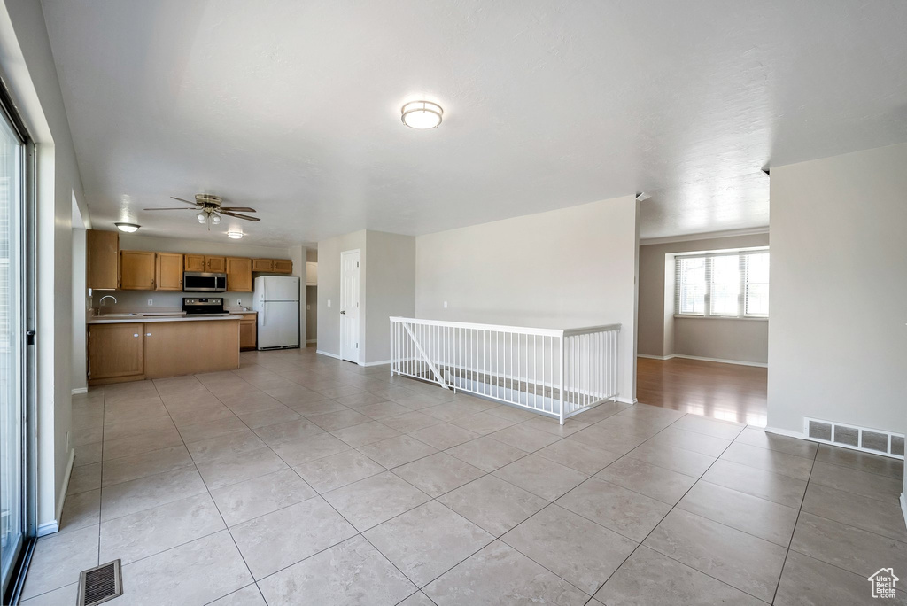 Unfurnished living room featuring light tile patterned floors, a ceiling fan, baseboards, and a sink