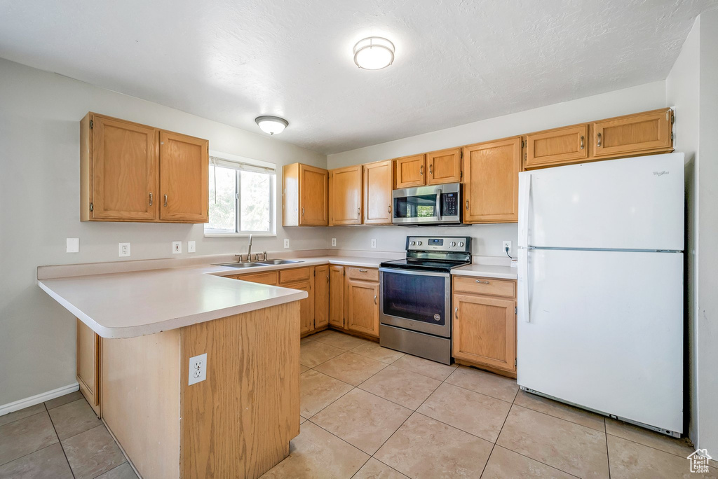 Kitchen with appliances with stainless steel finishes, a sink, a peninsula, light countertops, and light tile patterned floors