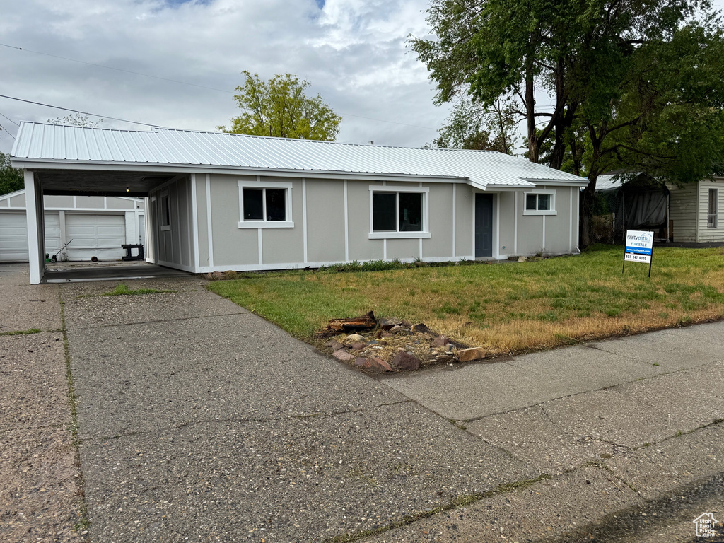 Ranch-style home with driveway, a front lawn, metal roof, and an attached carport