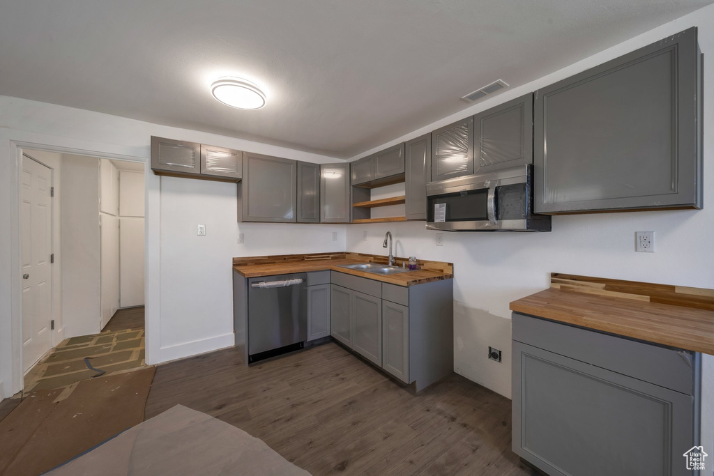 Kitchen featuring stainless steel appliances, butcher block counters, a sink, gray cabinets, and dark wood-style flooring