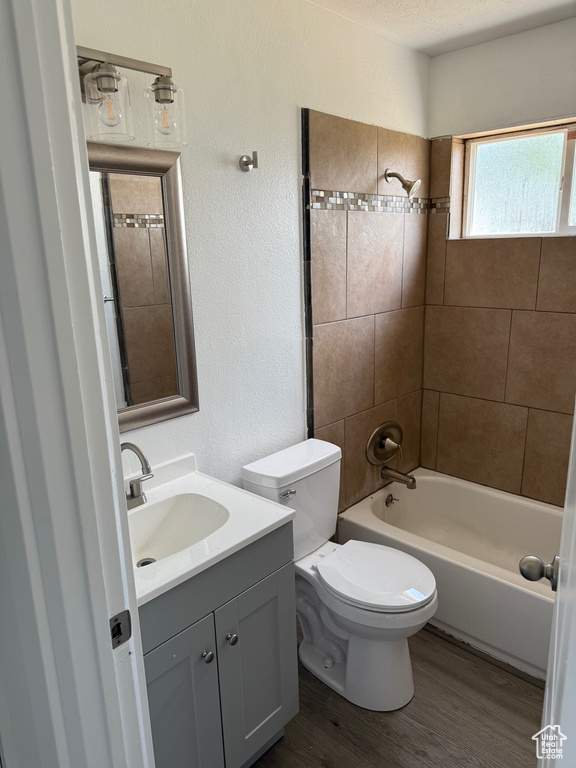 Bathroom featuring vanity, toilet, wood finished floors, a textured wall, and shower / bathtub combination