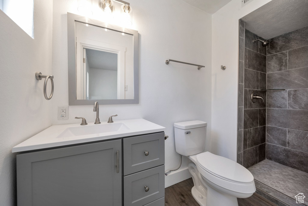 Full bathroom featuring toilet, tiled shower, vanity, wood finished floors, and baseboards