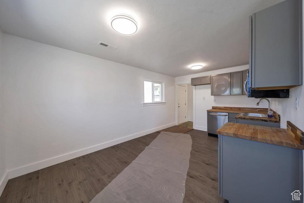 Kitchen featuring wooden counters, dishwasher, a sink, and baseboards