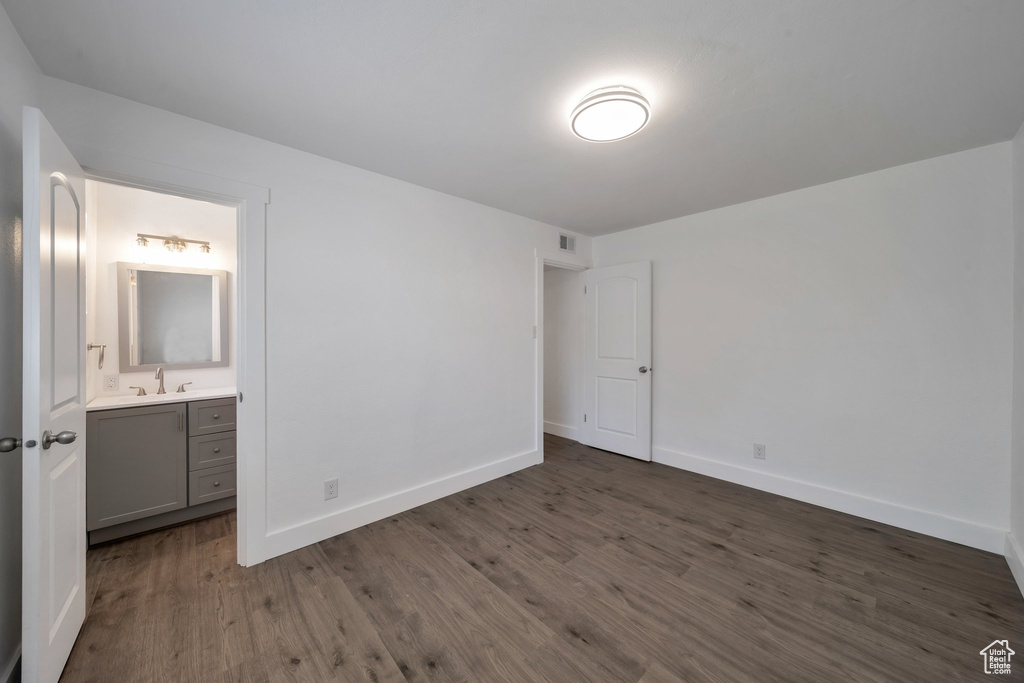 Unfurnished bedroom with dark wood finished floors, baseboards, connected bathroom, and a sink
