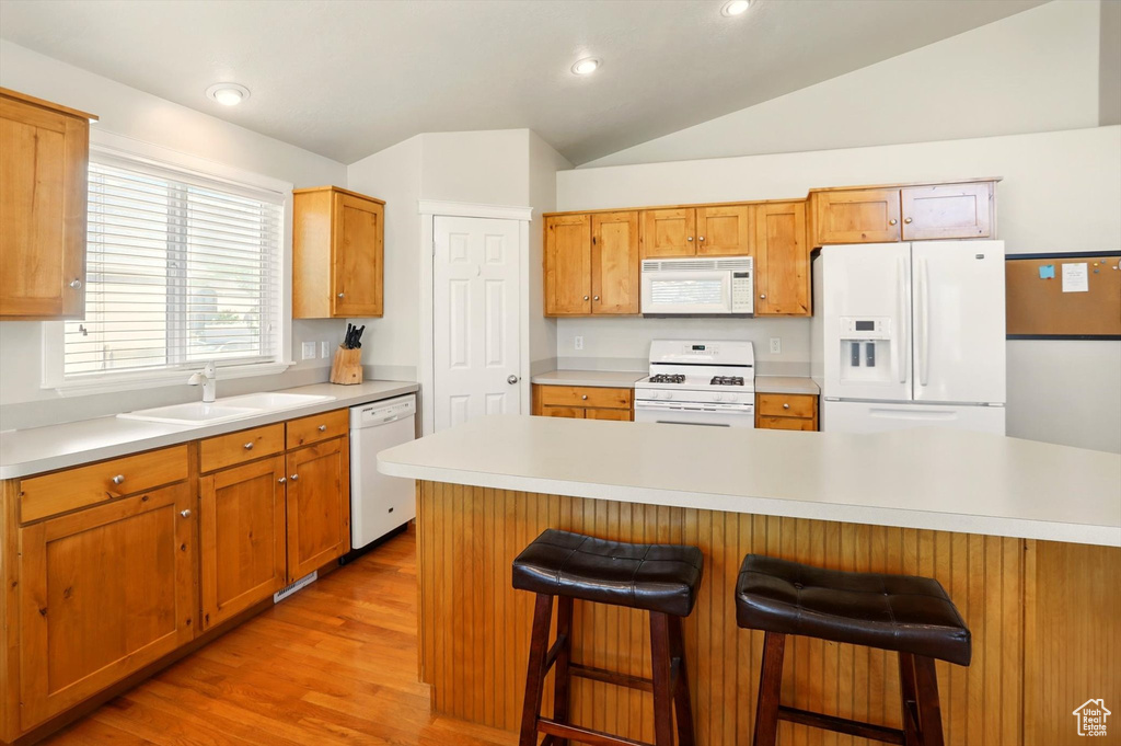 Kitchen featuring white appliances, a sink, light countertops, light wood-type flooring, and lofted ceiling