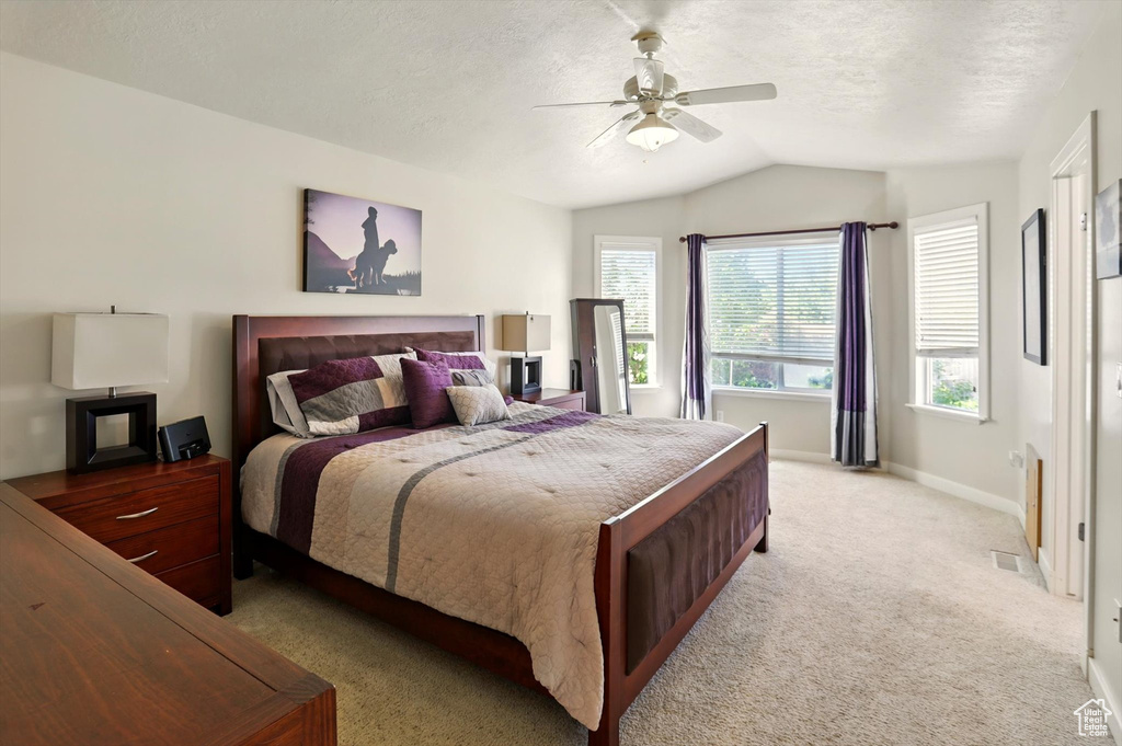 Bedroom with lofted ceiling, light carpet, baseboards, ceiling fan, and a textured ceiling