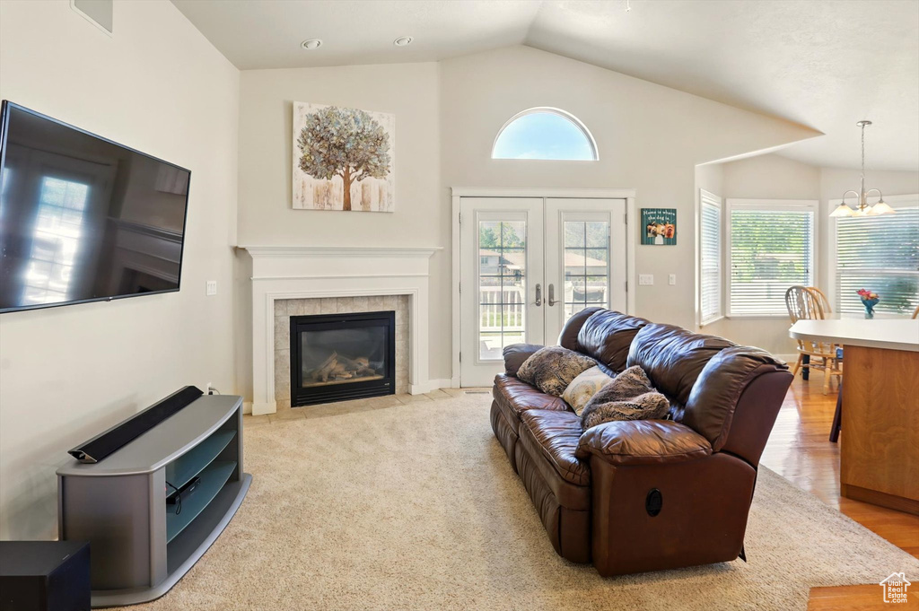 Living room featuring lofted ceiling, a tiled fireplace, a chandelier, and french doors