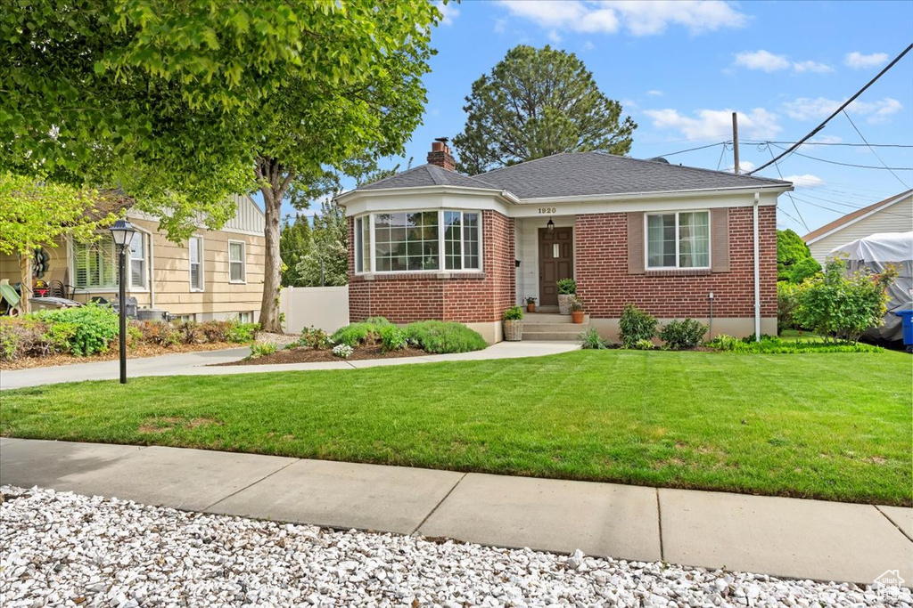 Bungalow-style home featuring brick siding, a chimney, and a front lawn