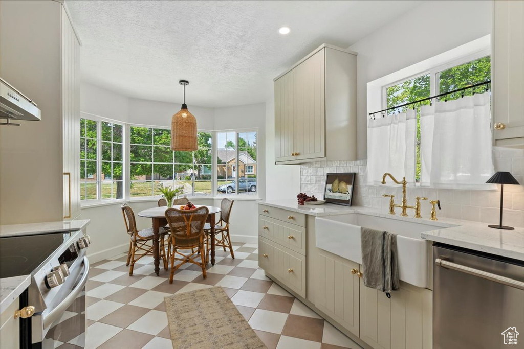 Kitchen featuring appliances with stainless steel finishes, light floors, plenty of natural light, backsplash, and a textured ceiling