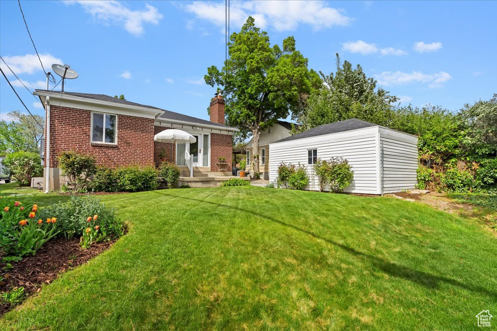 View of front of property featuring an outdoor structure, a front yard, brick siding, and a chimney