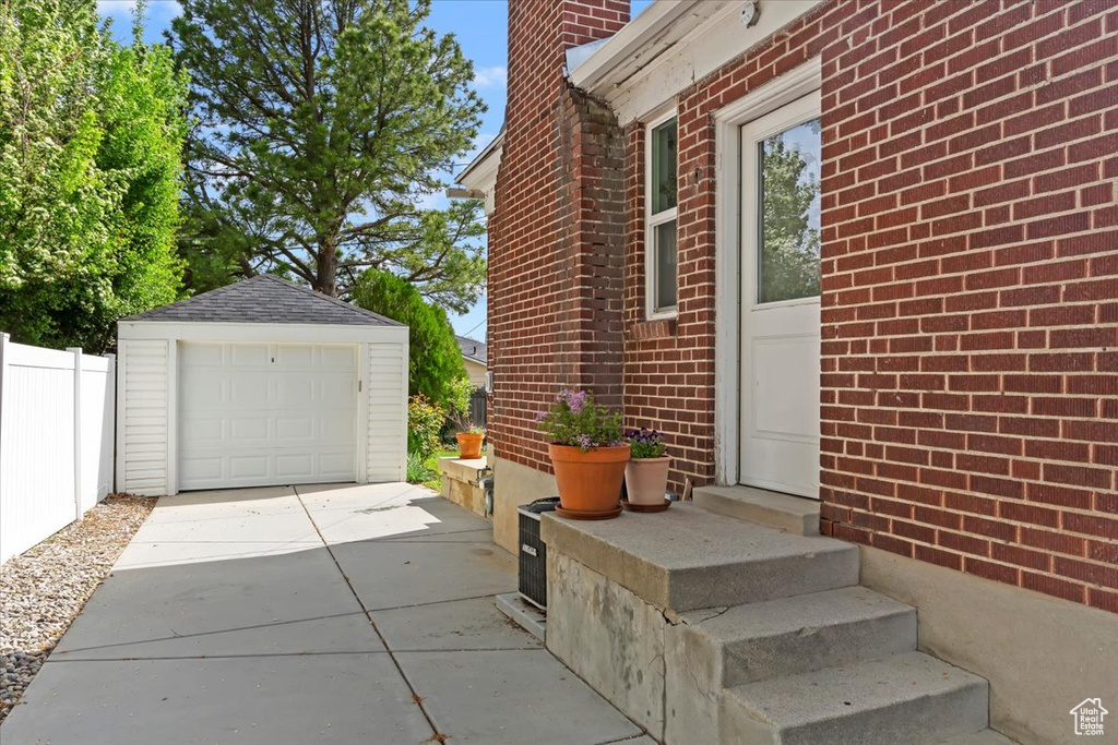 View of side of property featuring fence, driveway, an outbuilding, a detached garage, and brick siding