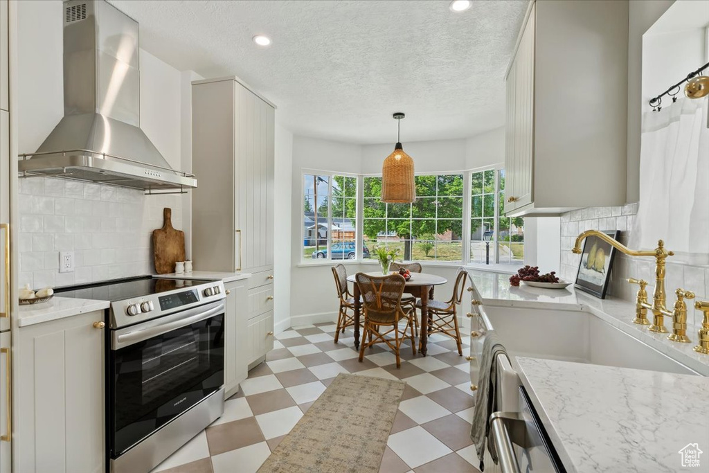 Kitchen featuring stainless steel electric range oven, light floors, wall chimney exhaust hood, a sink, and light stone counters