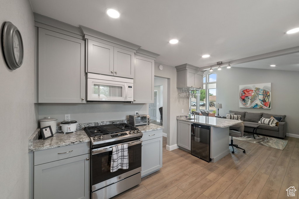 Kitchen with light wood-style flooring, gray cabinetry, stainless steel gas stove, white microwave, and open floor plan