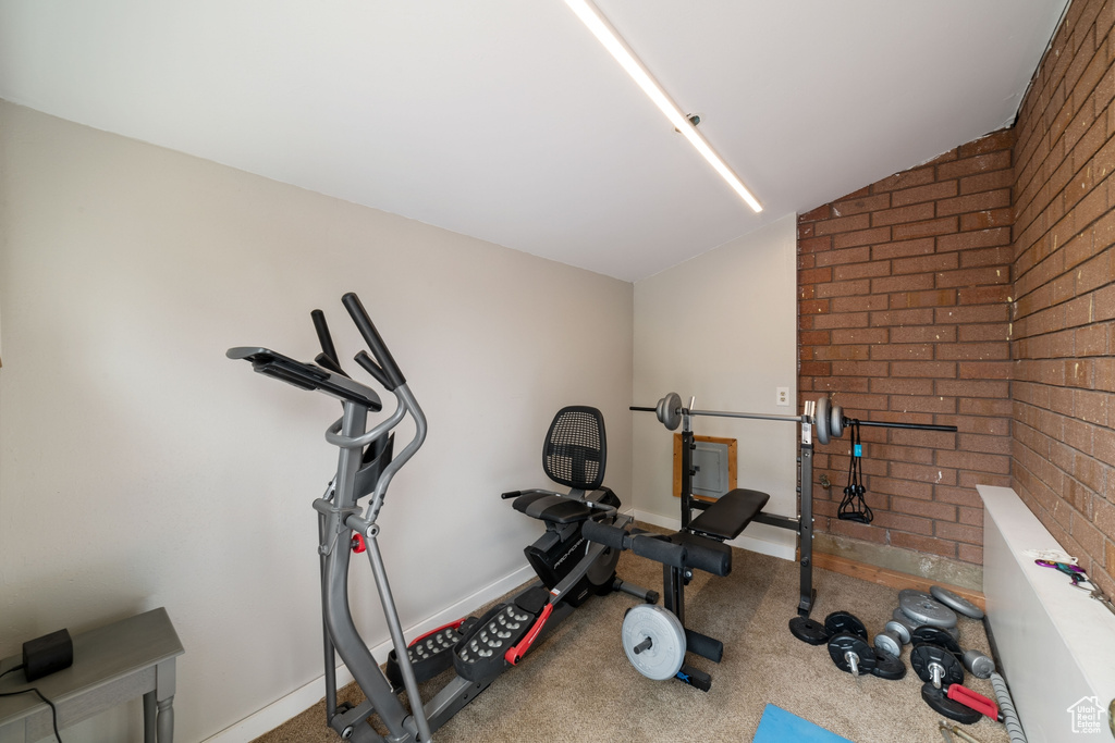 Workout room with lofted ceiling, carpet flooring, brick wall, and baseboards