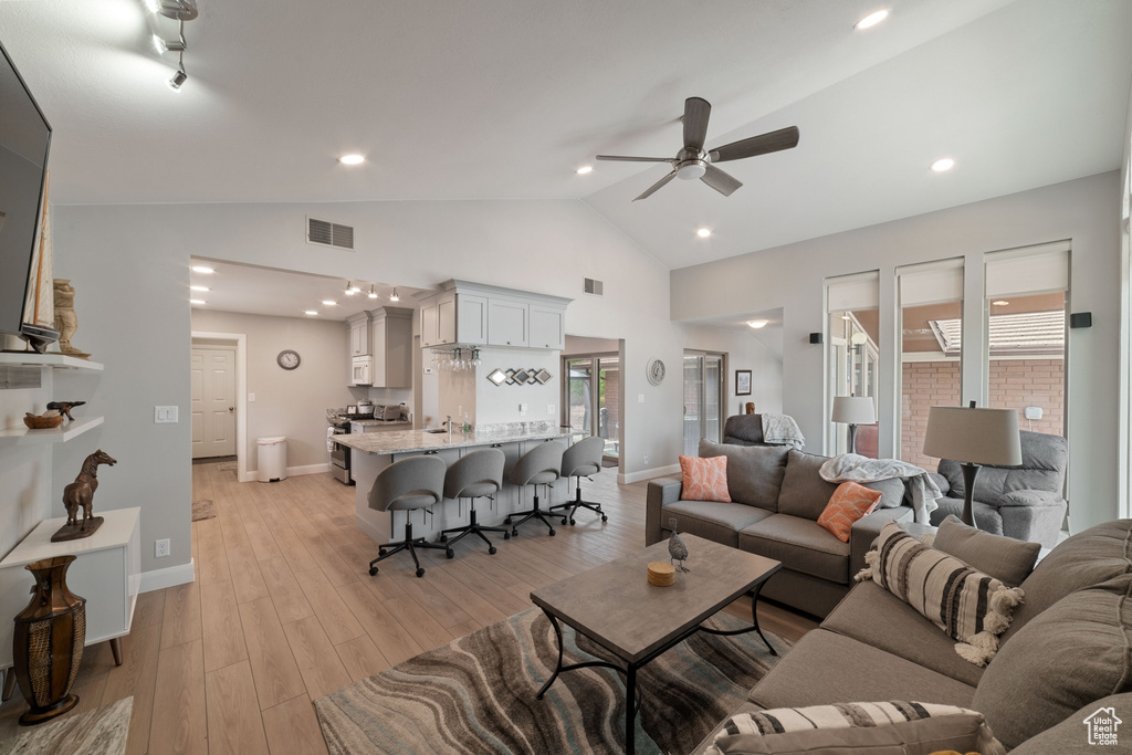 Living room with lofted ceiling, baseboards, light wood finished floors, ceiling fan, and visible vents