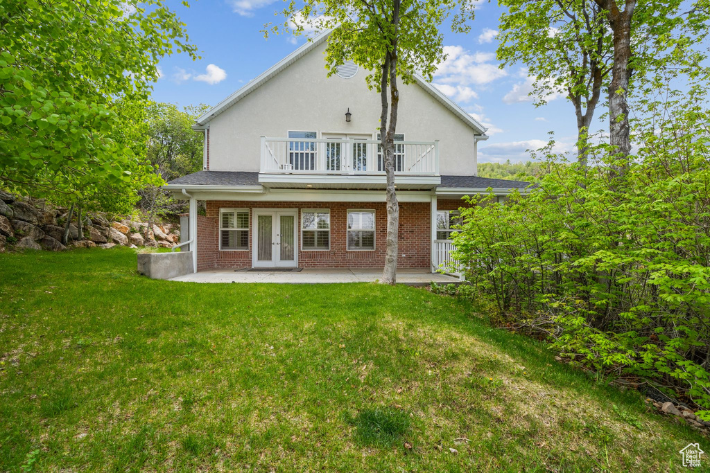Rear view of house featuring french doors, a balcony, a patio, a yard, and brick siding